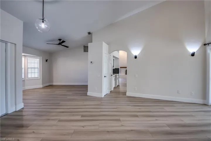 Spare room with ceiling fan, high vaulted ceiling, arched walkways, and light wood-style flooring