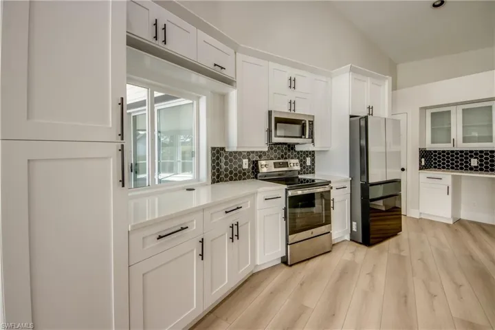 Kitchen featuring stainless steel appliances, white cabinetry, vaulted ceiling, tasteful backsplash, and light wood-style floors