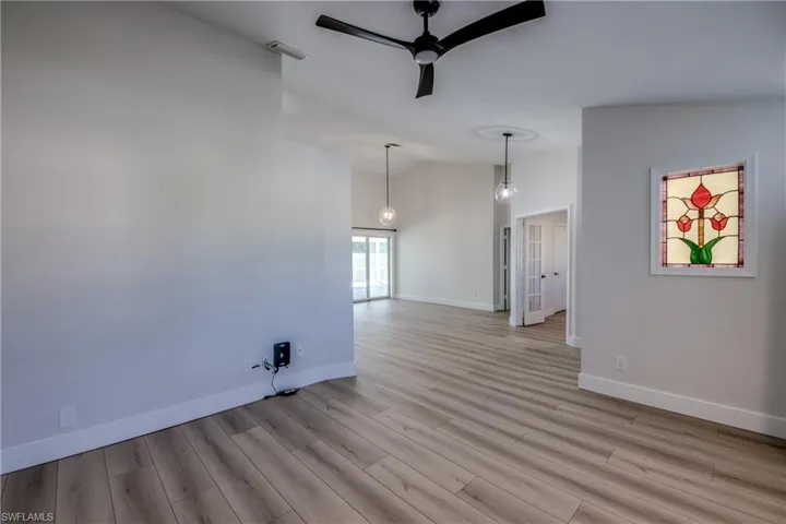 Empty room with ceiling fan, light wood-style floors, and high vaulted ceiling