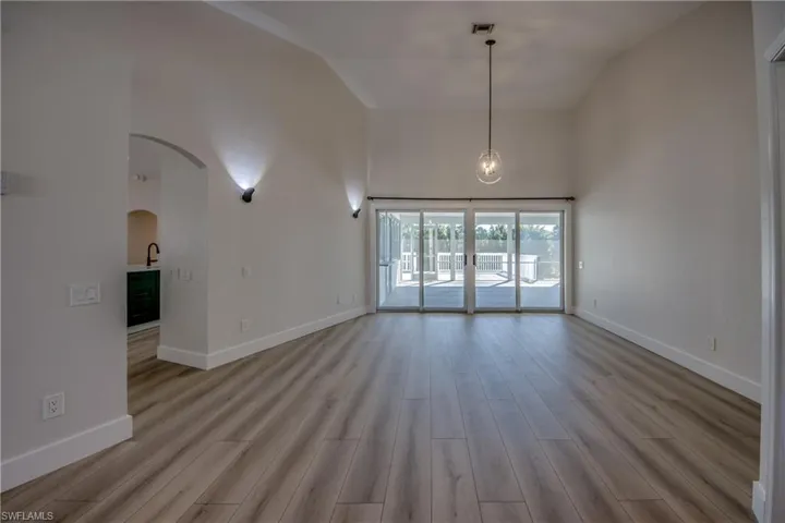 Unfurnished living room featuring high vaulted ceiling, arched walkways, and light wood-style flooring