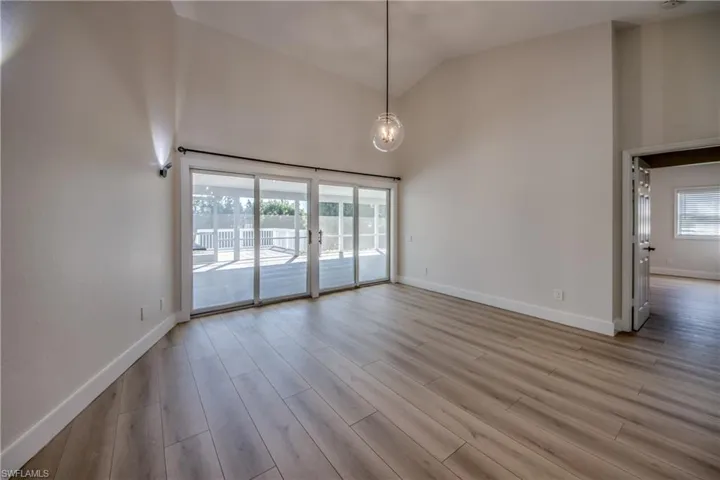 Empty room with high vaulted ceiling, light wood finished floors, and healthy amount of natural light