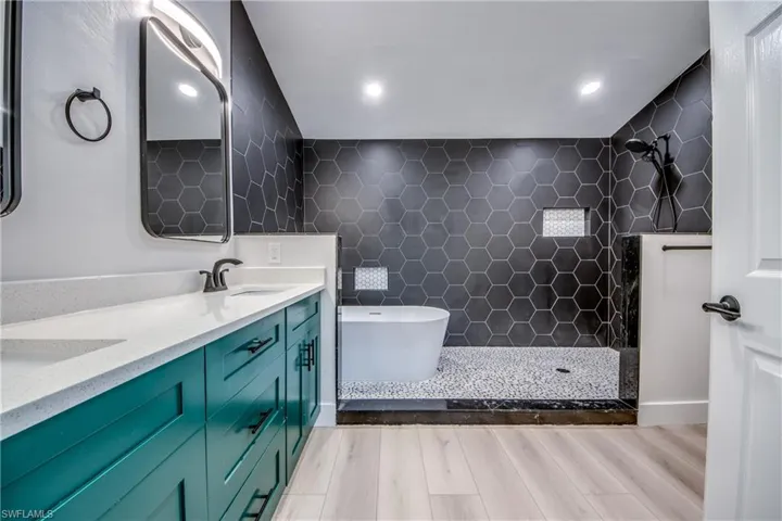 Bathroom with a freestanding bath, a walk in shower, double vanity, light wood-style floors, and tile walls
