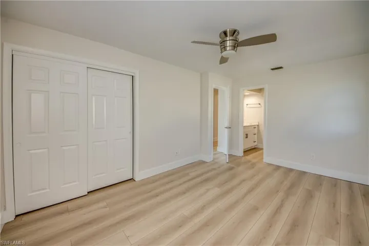 Unfurnished bedroom featuring a ceiling fan, light wood-style floors, a closet, and ensuite bath