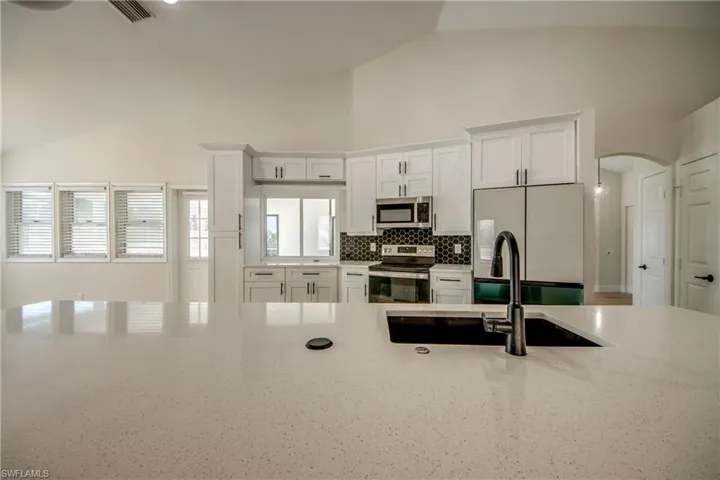 Kitchen with white cabinetry, appliances with stainless steel finishes, arched walkways, light stone counters, and high vaulted ceiling