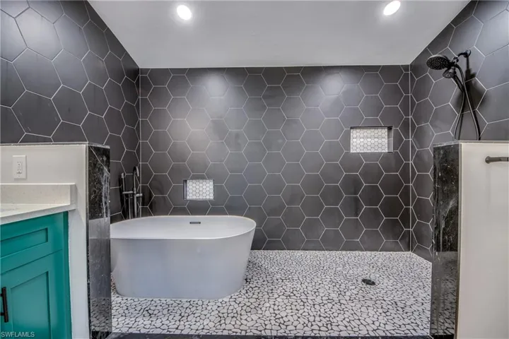 Bathroom featuring tile walls, tiled shower, a freestanding tub, vanity, and tile patterned flooring