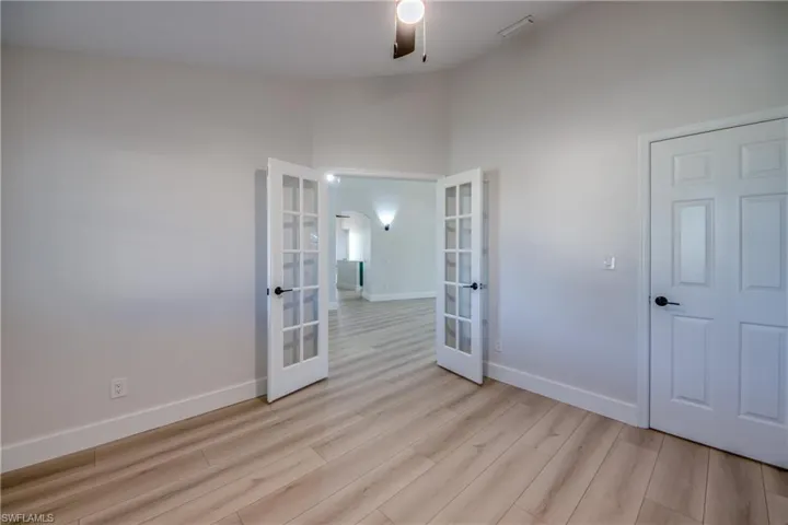 Empty room featuring french doors, light wood-style flooring, high vaulted ceiling, and ceiling fan