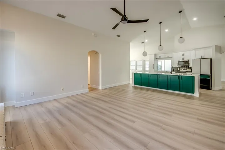 Unfurnished living room with high vaulted ceiling, ceiling fan, arched walkways, and light wood-style flooring