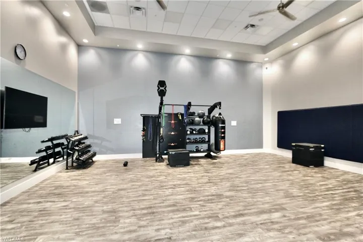 Workout room featuring wood finished floors, a towering ceiling, baseboards, a raised ceiling, and recessed lighting