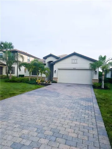 Ranch-style home featuring an attached garage, decorative driveway, a front lawn, stucco siding, and stone siding