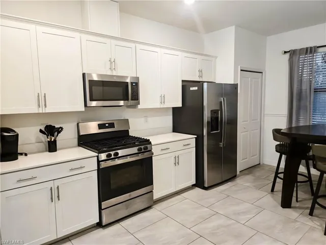 Kitchen featuring stainless steel appliances, light countertops, light tile patterned flooring, and white cabinets