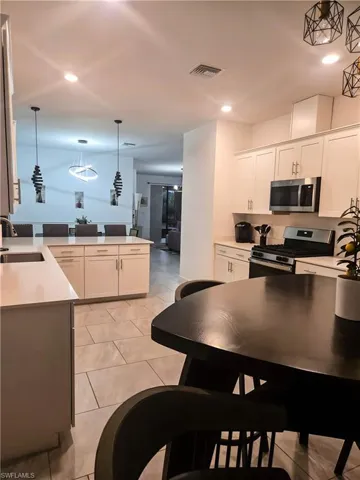 Kitchen featuring appliances with stainless steel finishes, a sink, white cabinets, hanging light fixtures, and light countertops