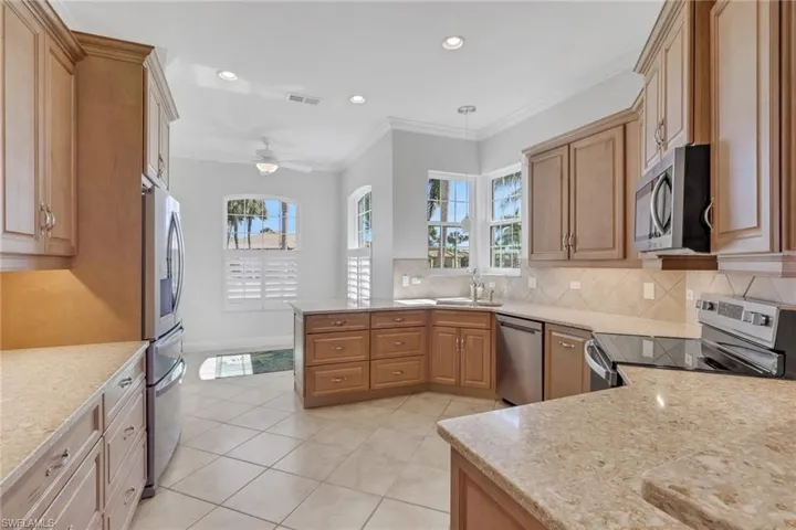 Kitchen featuring stainless steel appliances, ornamental molding, recessed lighting, light stone counters, and healthy amount of natural light