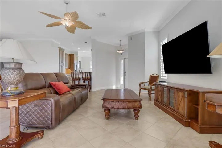 Living area featuring ornamental molding, a ceiling fan, light tile patterned flooring, and healthy amount of natural light