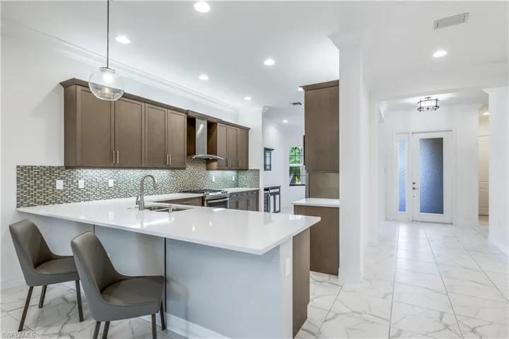 Kitchen featuring stainless steel range oven, wall chimney range hood, kitchen peninsula, pendant lighting, and decorative backsplash
