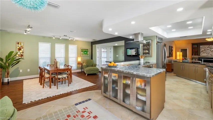 Kitchen featuring glass fronted cabinets, light tile patterned floors, dark stone countertops, open floor plan, and island exhaust hood