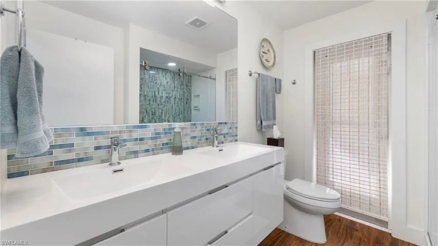 Full bathroom featuring double vanity, a stall shower, dark wood-style flooring, and backsplash