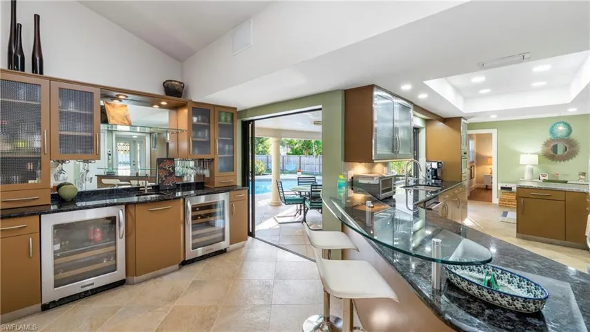 Kitchen featuring beverage cooler, dark stone countertops, wood finish cabinets, glass insert cabinets, and recessed lighting