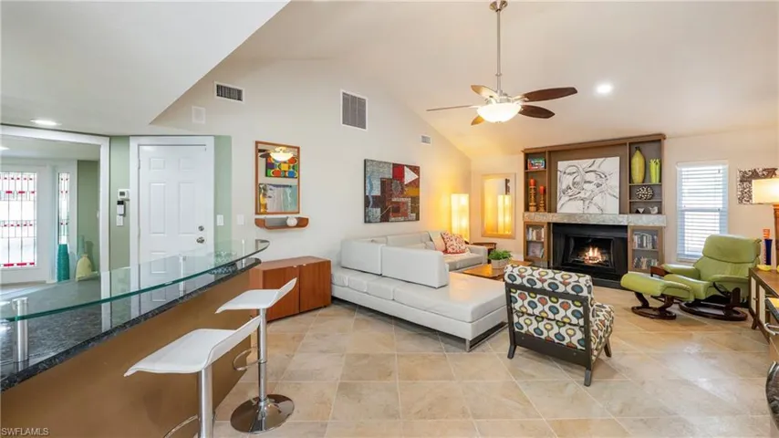 Living room featuring a lit fireplace, a ceiling fan, vaulted ceiling, recessed lighting, and light tile patterned flooring