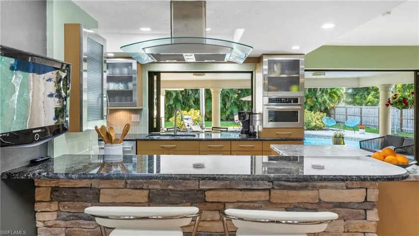 Kitchen featuring island range hood, stainless steel oven, dark stone counters, a breakfast bar area, and decorative backsplash