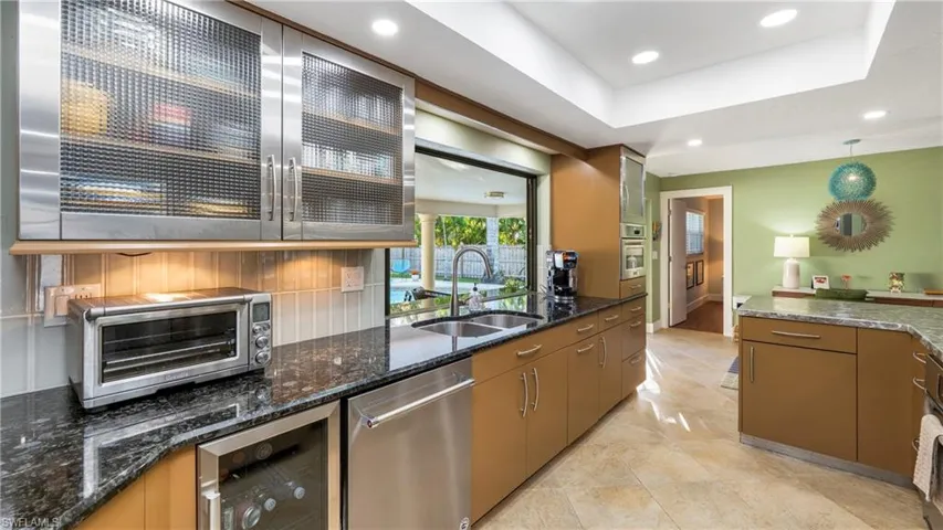 Kitchen featuring glass fronted cabinets, dark stone countertops, stainless steel appliances, beverage cooler, and a tray ceiling