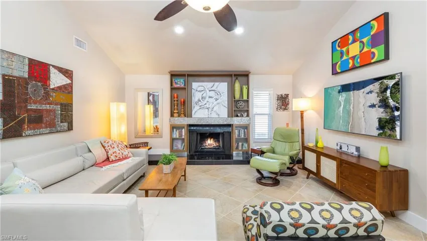Tiled living room featuring lofted ceiling, a ceiling fan, and a tiled fireplace