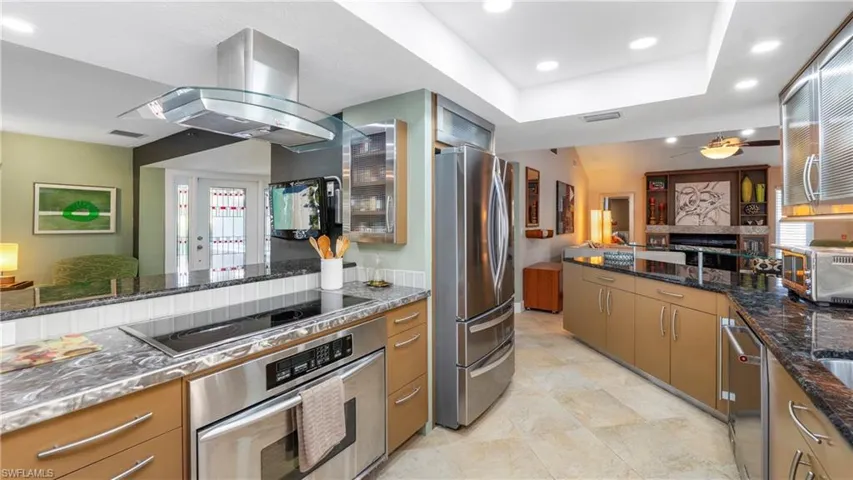 Kitchen with stainless steel appliances, dark stone countertops, open floor plan, island range hood, and recessed lighting