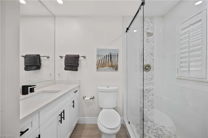 Bathroom with wood-type flooring, vanity with extensive cabinet space, walk in shower, and toilet