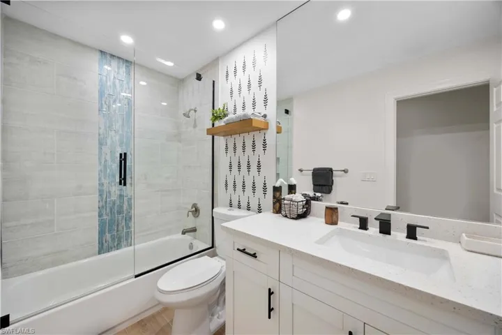 Full bathroom featuring combined bath / shower with glass door, toilet, and vanity