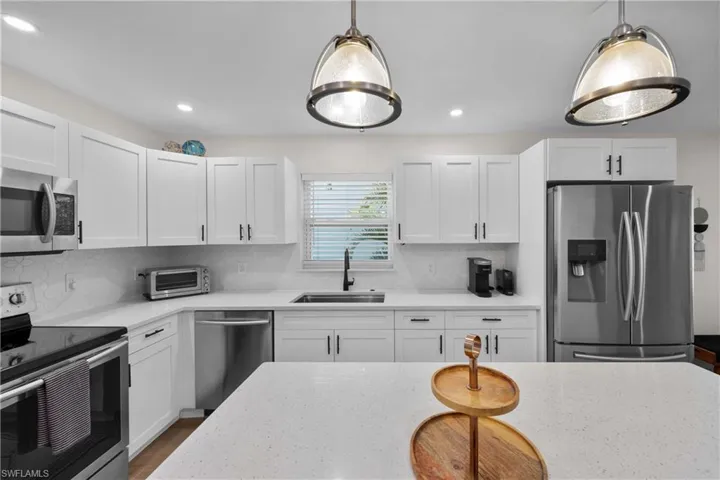 Kitchen with hanging light fixtures, appliances with stainless steel finishes, white cabinetry, and tasteful backsplash