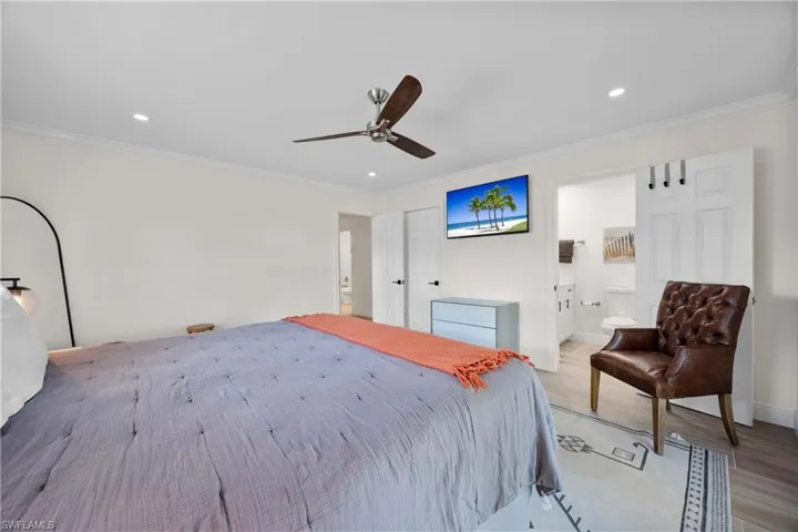 Bedroom with connected bathroom, ceiling fan, light wood-type flooring, and crown molding