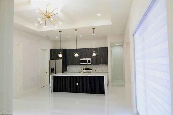 Kitchen with an island with sink, modern cabinets, light stone counters, stainless steel appliances, and hanging lights