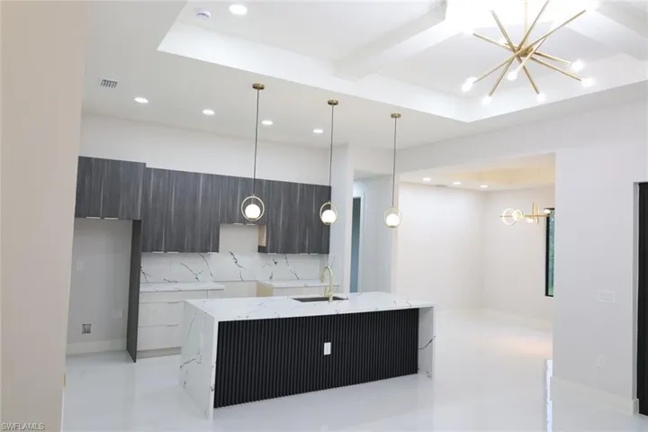 Kitchen with modern cabinets, a chandelier, light stone counters, beam ceiling, and tasteful backsplash