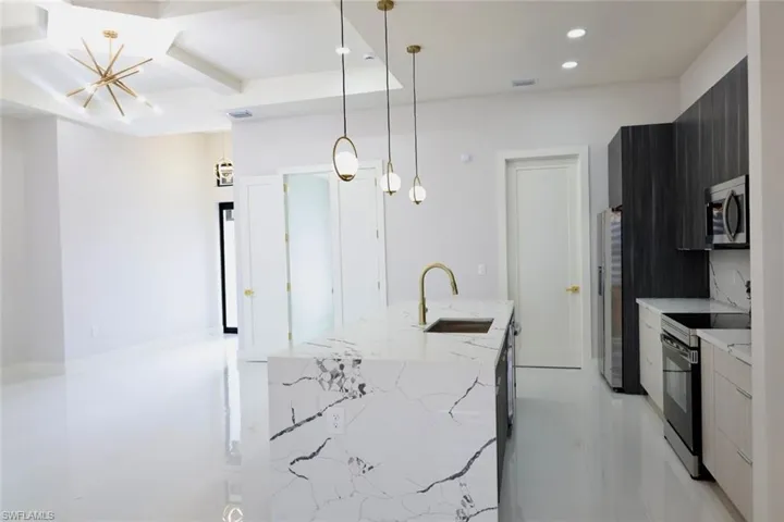 Kitchen with modern cabinets, light stone countertops, a kitchen island with sink, electric stove, and stainless steel microwave