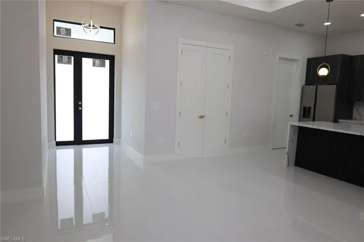 Kitchen with pendant lighting, stainless steel fridge, light stone counters, dark cabinets, and light tile patterned floors