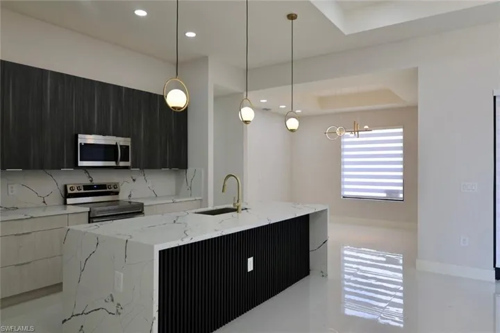 Kitchen featuring modern cabinets, light stone countertops, stainless steel appliances, a center island with sink, and pendant lighting