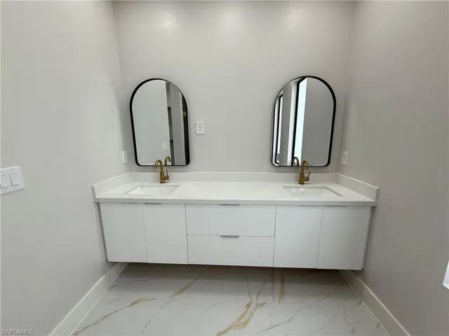 Full bath featuring double vanity and light marble finish flooring
