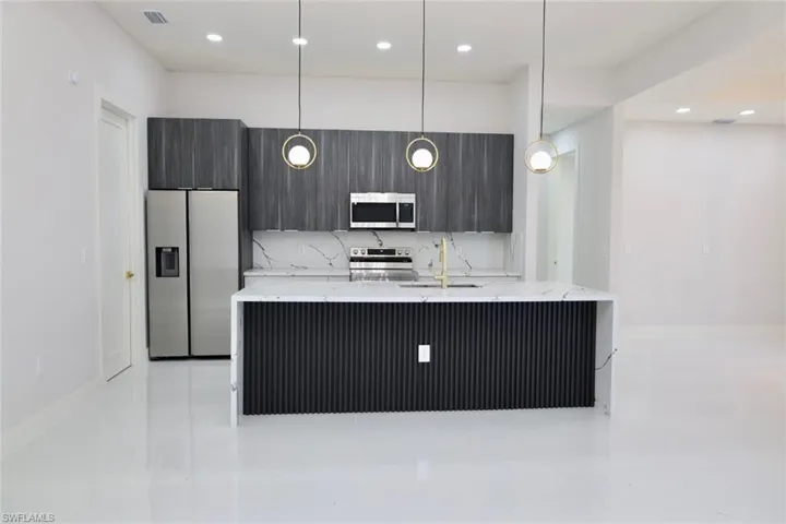 Kitchen featuring light stone counters, stainless steel appliances, an island with sink, modern cabinets, and decorative light fixtures