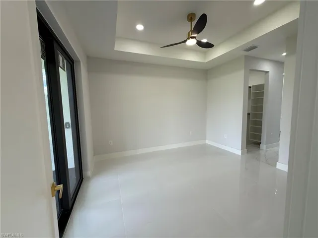 Empty room featuring a tray ceiling, light tile patterned flooring, a ceiling fan, and recessed lighting