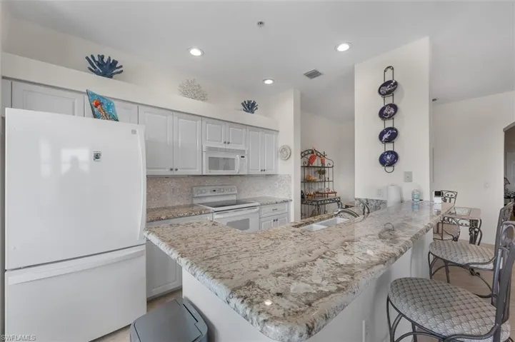 Kitchen featuring decorative backsplash, white appliances, light stone countertops and a kitchen breakfast bar