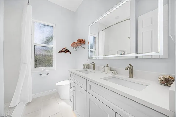 Dual-sink vanity with white cabinetry, light-toned GRANITE-surface countertop, integrated LED-backlit mirror, and brushed-finish fixtures