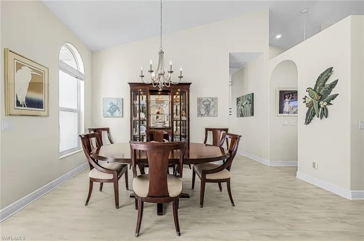 Dining area featuring vaulted ceilings, arched architectural detailing, wood-finish flooring, a multi-arm chandelier, and an arched window