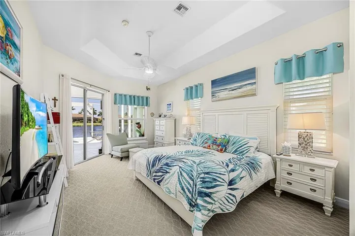 Tray ceiling featuring a recessed center, neutral carpeting, glass sliding doors, and windows equipped with plantation-style shutters