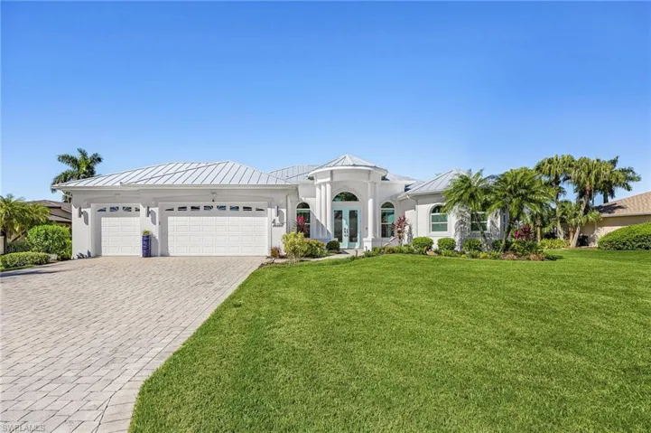 Single-story exterior featuring a metal roof, paver driveway, three-car garage, arched entryway with columns, and landscaping
