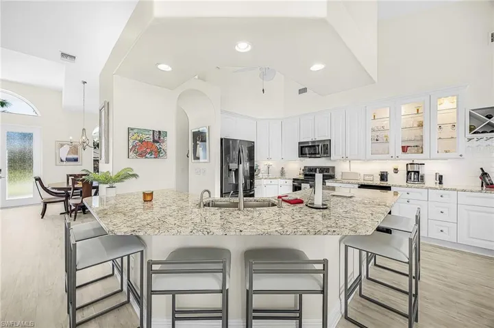 Kitchen featuring a peninsula with a stone countertop, white cabinetry with glass-front display uppers, stainless steel appliances, recessed lighting, and LVP flooring.