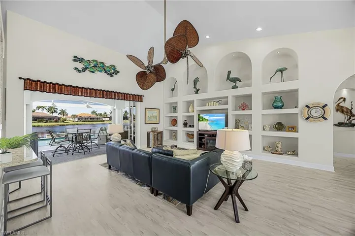 Vaulted ceilings featuring a multi-blade ceiling fan, expansive wall of custom built-in shelving with arched niches, and LVP flooring