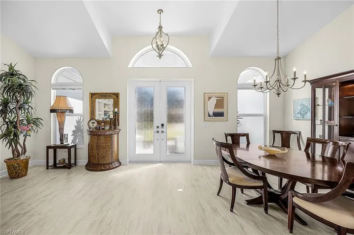 Double front doors with glass detailing, arched windows, tray ceiling, and dual hanging chandeliers