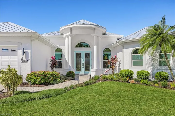 Stucco exterior featuring a metal roof, arched windows, and a columned entryway with a paved driveway and walkway