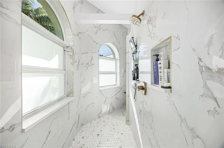 Walk-in shower featuring floor-to-ceiling 24" x 48" Porcelain tile, arched windows, built-in recessed shelving, a pebble-finish fshower loor, and Delta Champagne Bronze metallic-finish hardware