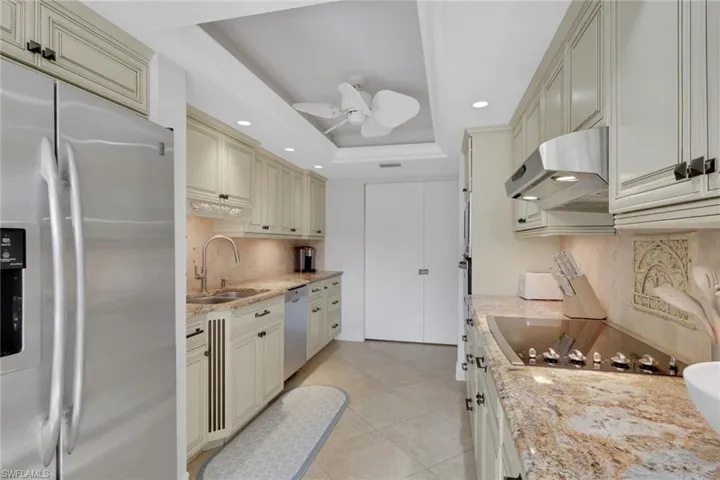 Kitchen featuring cream cabinetry, stainless steel fridge with ice dispenser, light stone counters, a tray ceiling, and recessed lighting