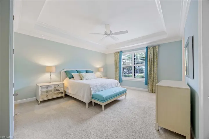 Bedroom featuring a raised ceiling, carpet floors, crown molding, and a ceiling fan